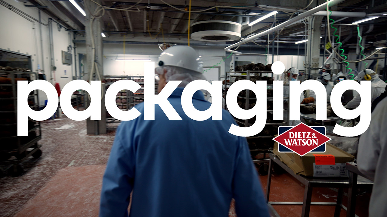 Dietz CEO, Louis, walks through the packaging facility where dozens of employees are working in front of large industrial packaging machines.