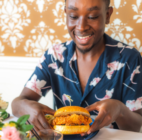 Josh is smiling while holding what appears to be a chicken sandwich.